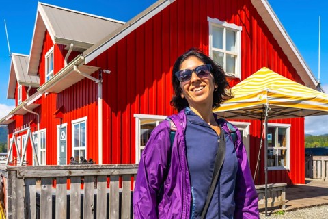 Happy tourist wearing sunglasses and purple jacket smiling in front of a vibrant red building in