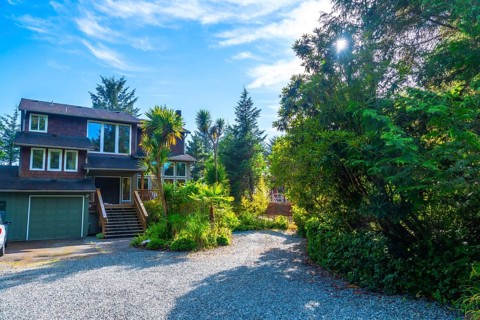 Lush green vegetation surrounds a charming two story house with a gravel driveway and attached