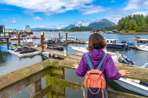Young woman with a backpack enjoying the scenic view of boats in tofino harbor on a sunny summer