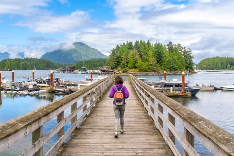 Female tourist with backpack walking down a wooden pier in tofino, british columbia, with boats,