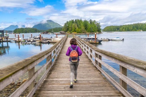 Female tourist walking down a wooden pier in tofino, british columbia, with boats and lush islands