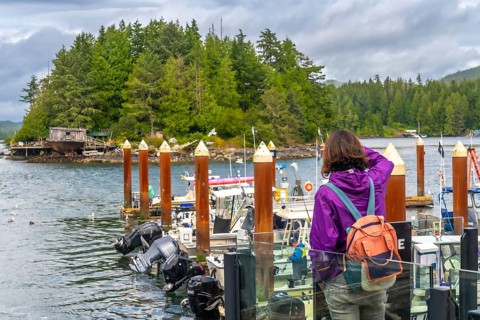 Tourist in a purple jacket and backpack capturing photos of the scenic tofino harbor, featuring