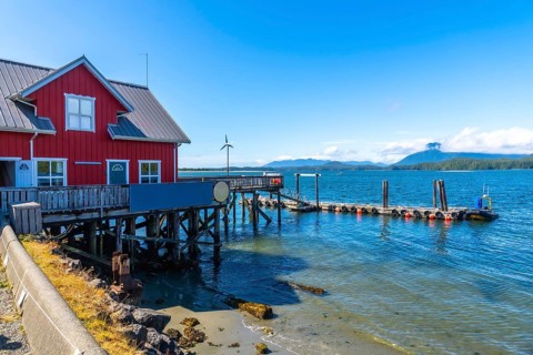 Calm, clear blue water lapping against the shore complements a vibrant red wooden building and pier