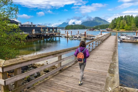 Female tourist with backpack walking down a wooden pier in tofino, british columbia, canada,