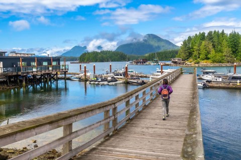 Tourist with backpack walking down a pier in tofino, british columbia on a beautiful summer day