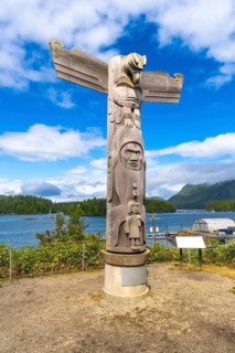 Wooden totem pole featuring intricate carvings of a thunderbird and other figures, rising against a