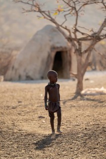 Child in front of Himba hut, traditional Himba village in the savanna, arid landscape, Kaokoveld,