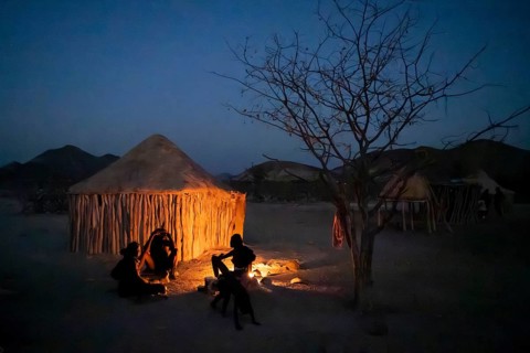 Himba at the campfire in the evening, night view, Himba huts, traditional Himba village in the
