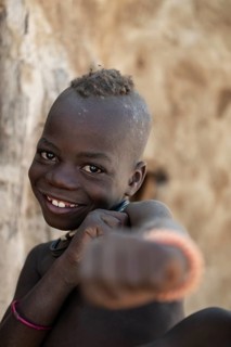 Happy Himba child punching funny at the camera, traditional Himba village, Kaokoveld, Kunene,