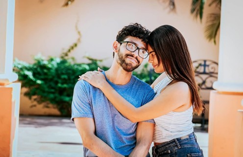 Attractive girl tenderly hugging her boyfriend outdoors. Girl hugging her boyfriend while he smiles