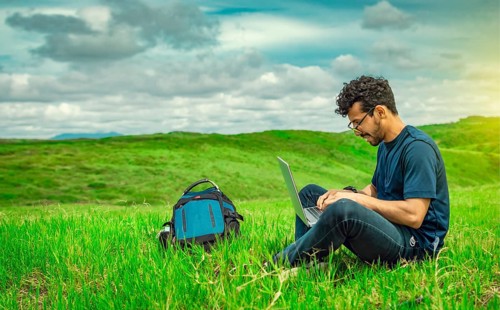 Smiling freelancer young man with laptop working from the field. Close up of man sitting on green