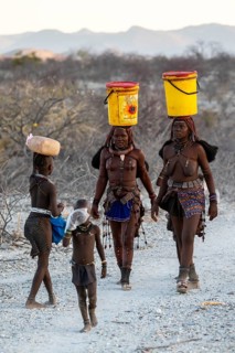 Himba woman and children run to fetch water with canisters through dry countryside, traditional
