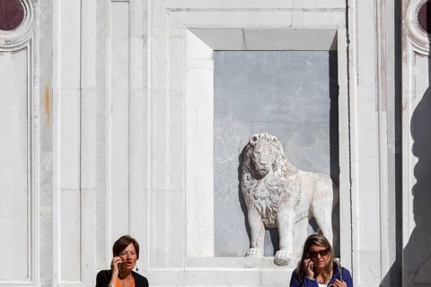 2 woman make phone calls in front of the lion relief on the façade of the Scuola Grande di San