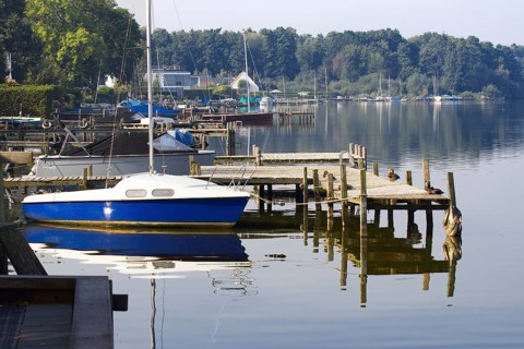 A sailboat anchors on a wooden pier in a quiet harbor on Lake Steinhude, Steinhude