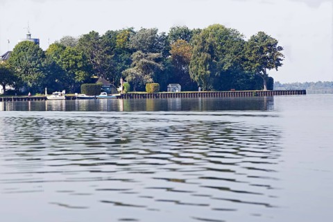 Tranquil landscape (Wilhelmstein Island) on the lakeshore with a dense row of trees and boats on