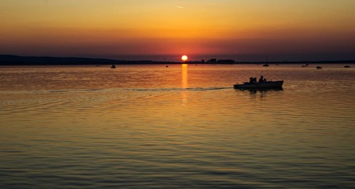 Boat over calm waters at sunset, orange dusk, Steinhude Steinhuder Meer