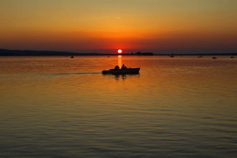 Sunset with boat in the middle of the lake, calm waters, peaceful view, Steinhude Steinhuder Meer