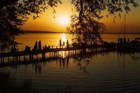 Sunset behind trees with silhouettes of people at pier, quiet landscape, Steinhude, Steinhuder Meer