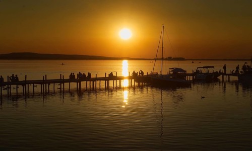 Sunset over the Steinhuder Meer with people on a pier, reflecting sailboats, peaceful, Steinhude