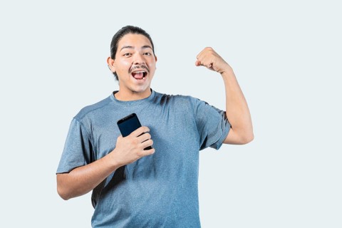 Happy young man holding phone celebrating isolated. Winner guy celebrating with his phone isolated