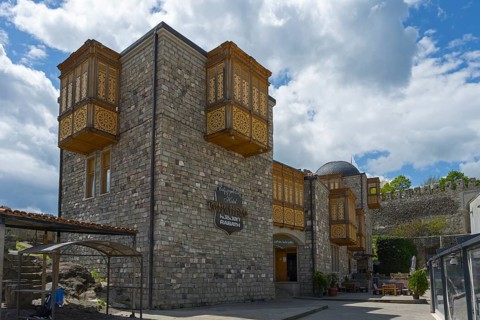 A historic building with intricately decorated wooden balconies against a cloudy sky, Rabati