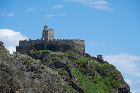 Medieval castle on a steep hill with stone walls and a watchtower under a blue sky, Rabati