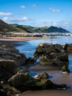 Castlepoint Beach, ocean, sandy beach, rocks, mountains. Castlepoint, Wairarapa Coast, Wellington