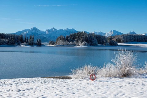 Snowy lake with mountains in the background under blue sky, Forggensee near Roßhaupten, Ostallgäu,