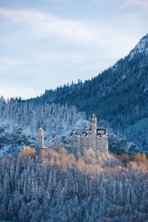 Majestic Neuschwanstein Castle in winter surrounded by snow-covered forest and mountain landscape,