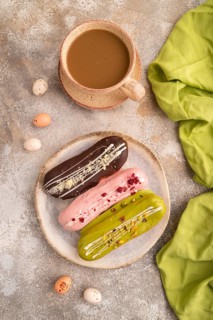 Glazed Eclairs on brown concrete background and green linen textile, cup of coffee, top view, flat