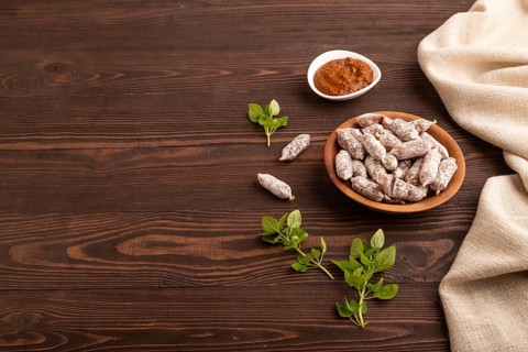 Small smoked Chicken sausages in wooden bowl on brown wooden background and linen textile. side
