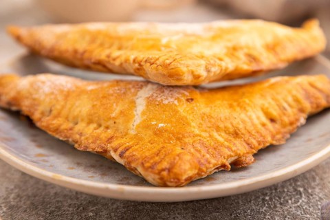 Triangles Pie, Puff Pastry, Samsa with cherry jam on brown concrete background and linen textile,