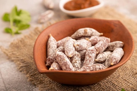 Small smoked Chicken sausages in clay bowl on brown concrete background and linen textile. side