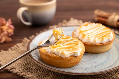 French lemon tart with meringue on brown wooden background, cup of coffee, linen textile, side