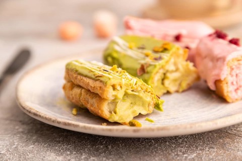 Glazed Eclairs on brown concrete background and green linen textile, cup of coffee, side view,