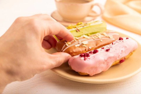 Glazed Eclairs on white wooden background and orange linen textile with hand, cup of coffee, side
