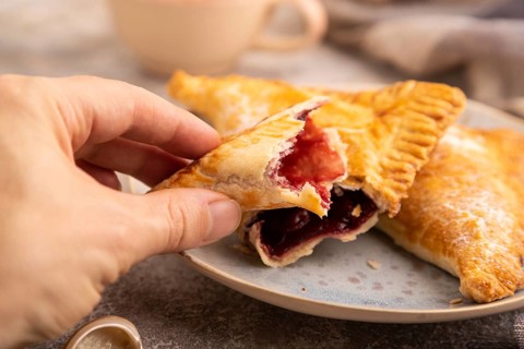 Triangles Pie, Puff Pastry, Samsa with cherry jam on brown concrete background and linen textile