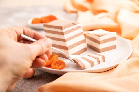Cocoa and milk jelly with dried apricots with hand on brown concrete background and orange textile,