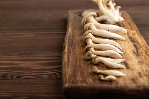 Raw Oyster mushroom, Pleurotus ostreatus on cutting board on brown wooden background. Side view,