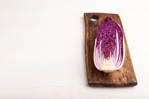 Purple Chinese cabbage on cutting board on white wooden background, side view, copy space,