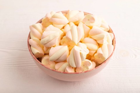 Orange and pink marshmallow in ceramic bowl on white wooden background, side view, copy space,