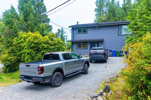 Modern two story gray house featuring a pickup truck and suv parked in a gravel driveway,