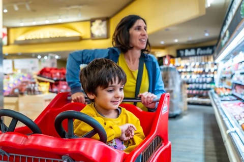 Mother pushing a shopping cart with her son sitting inside, enjoying their grocery shopping