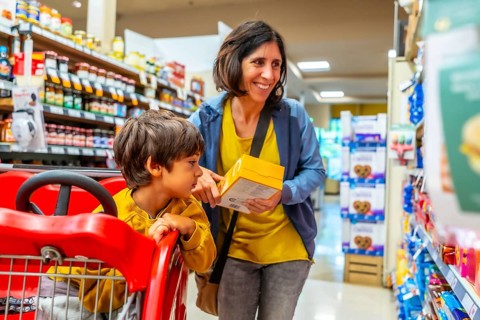 Smiling mother holding a yellow box while shopping with her son sitting in a shopping cart in a