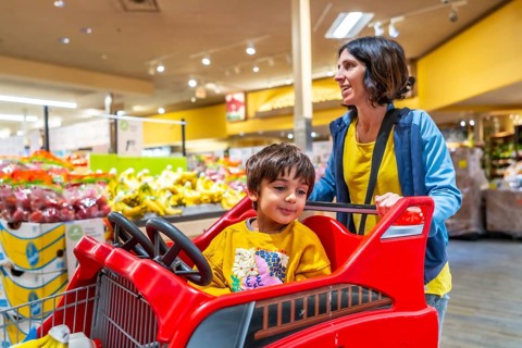 Mother joyfully pushing her son in a specially designed shopping cart resembling a truck during