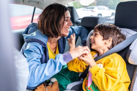 Mother turning back to her son, sitting in a child car seat, sharing joyful moments and laughter