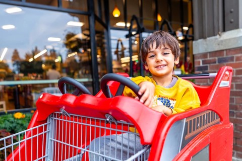 Smiling preschooler having fun sitting in a special children's shopping cart shaped like a