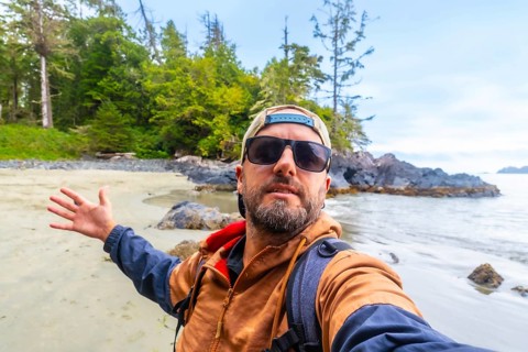 Tourist with sunglasses and baseball cap taking a selfie on chesterman beach, showing the beautiful