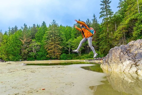 Energetic backpacker leaping across a tide pool on mackenzie beach in tofino, showcasing the
