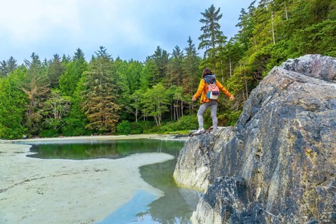Female hiker with a backpack standing on rocks with outstretched arms, savoring the breathtaking